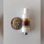 Flüssige Diamanten vs. lebendes Harz vs. Destillat: eine 510-Vape-Kartusche, gefüllt mit bernsteinfarbenem Cannabisöl, daneben ein Viertel für die Waage