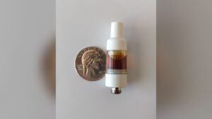 Flüssige Diamanten vs. lebendes Harz vs. Destillat: eine 510-Vape-Kartusche, gefüllt mit bernsteinfarbenem Cannabisöl, daneben ein Viertel für die Waage